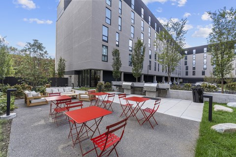 A modern building with a patio area featuring red chairs and tables.