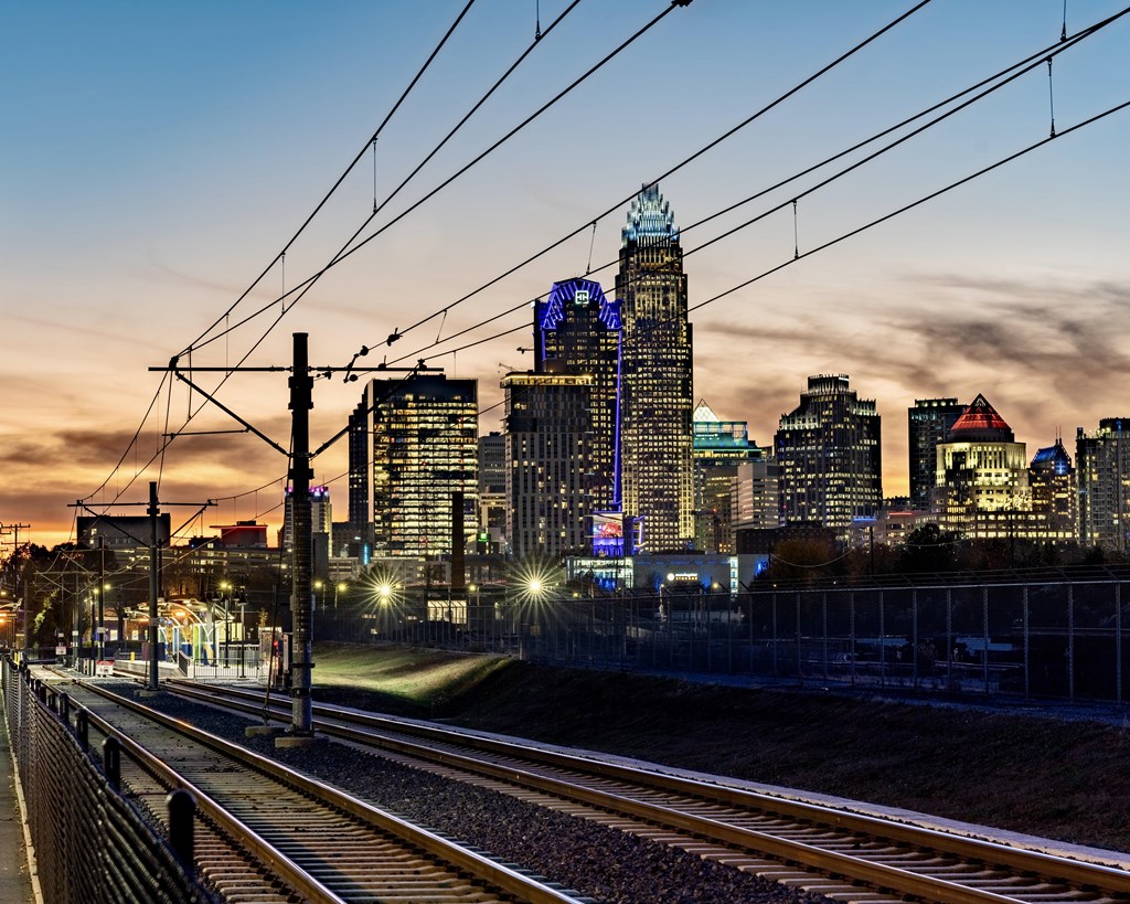 A train track with power lines and a city skyline in the background.