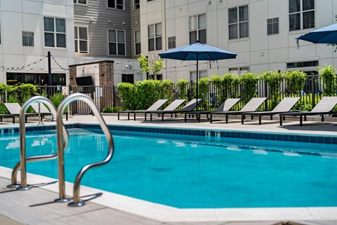 A pool with a diving board and lounge chairs.
