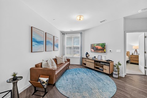 A living room with a brown couch, a blue rug, and a painting on the wall.