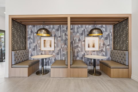 A modern lounge area with two booths, each with a table and a bench, and a patterned wallpaper.