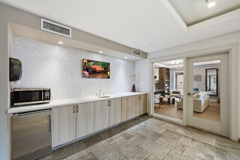 A modern kitchen with a stainless steel refrigerator and microwave, a sink with a faucet, and a tiled floor.