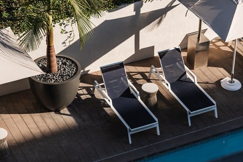 Three lounge chairs are arranged on a wooden deck next to a pool.