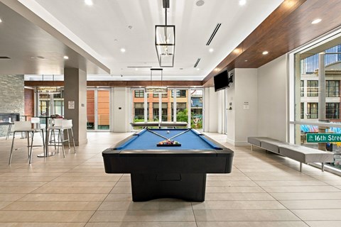 A pool table is in the middle of a room with a bar and a TV.