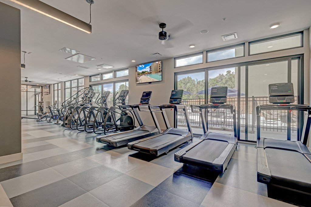 a large fitness room with cardio machines and a flat screen tv