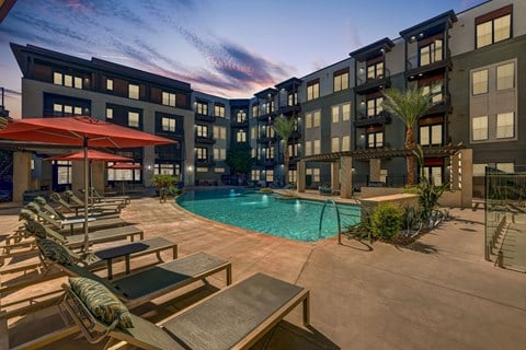 A pool area with lounge chairs and umbrellas in front of apartment buildings.