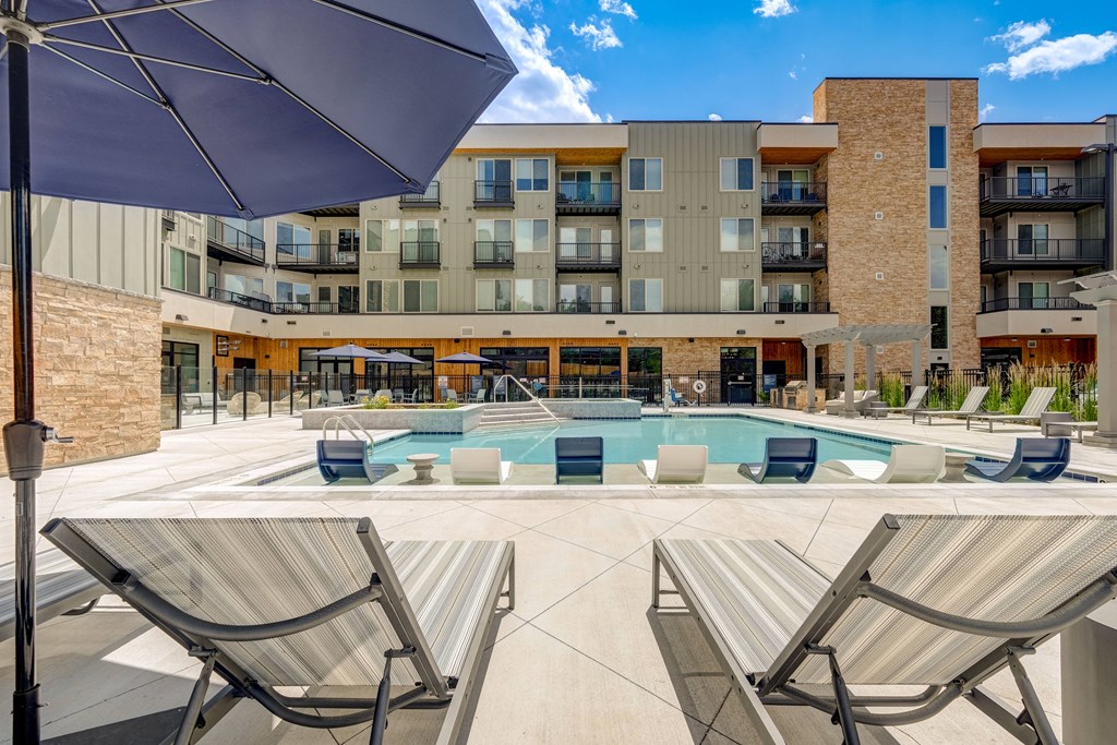 a pool with lounge chairs and umbrellas in front of a building