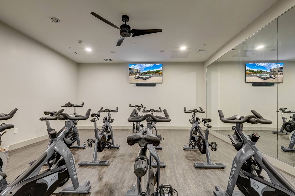 a spacious fitness room with cardio bikes and flat screen tvs