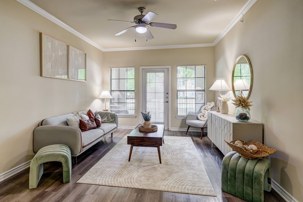 A living room with a grey couch, a coffee table, a green bench, a white radiator, a round mirror, and a ceiling fan.