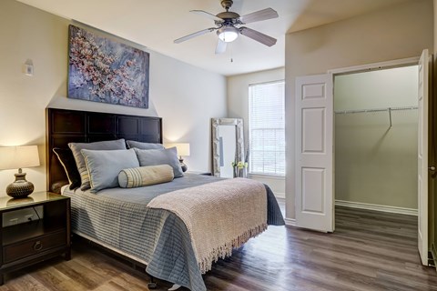 A bedroom with a bed, a ceiling fan, and a painting on the wall.