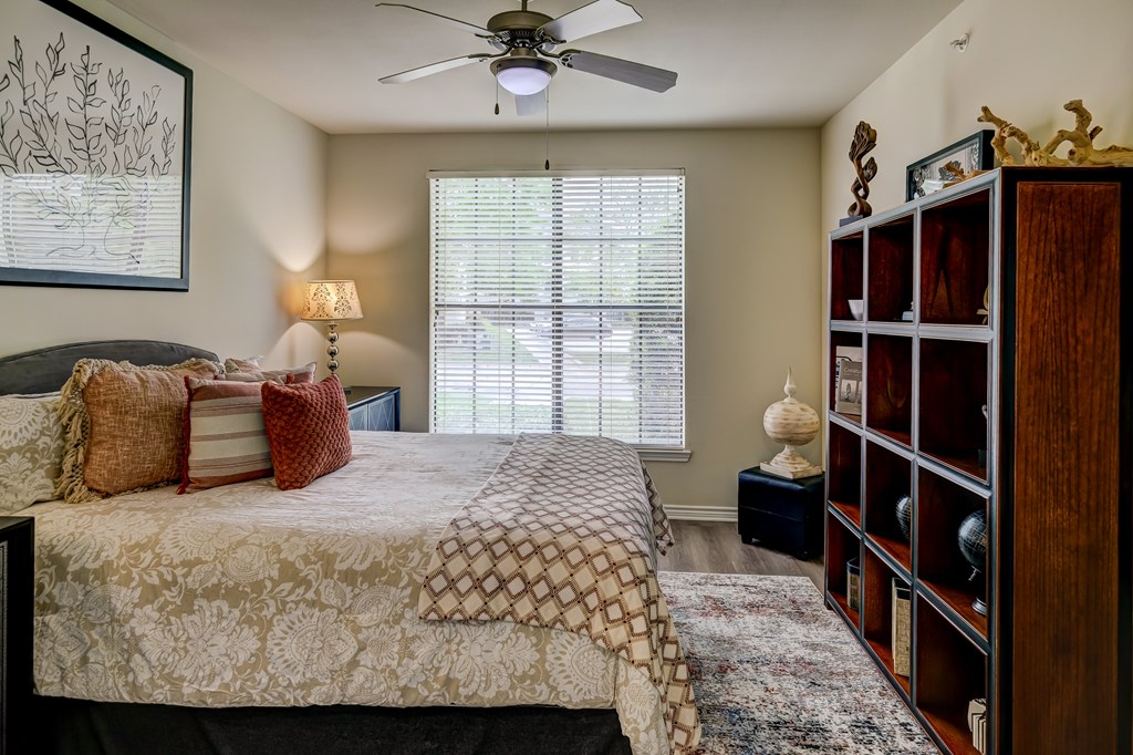 A bedroom with a bed, a fan, and a window with blinds.