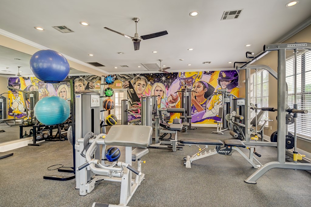 A gym with a variety of equipment including a weight bench, a blue exercise ball, and a ceiling fan.
