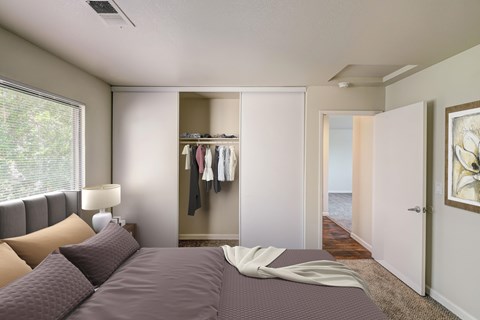 A bedroom with a large bed and a closet with clothes hanging.