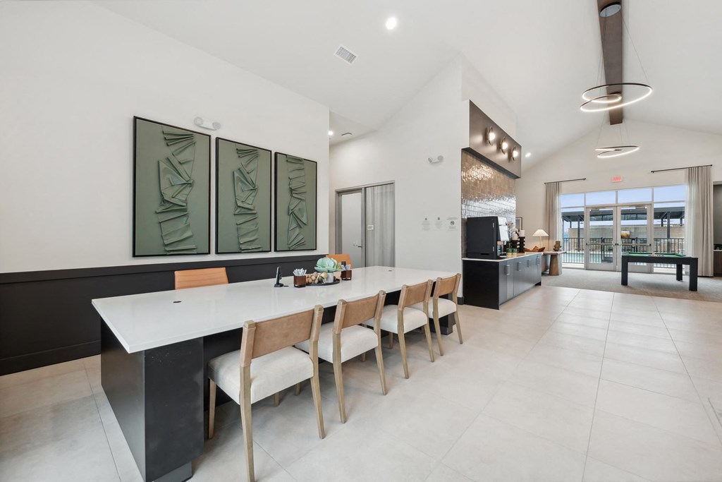 A modern kitchen with a long white table and chairs.