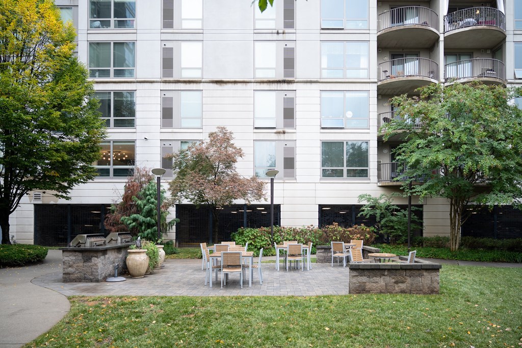 a patio with a fire pit and chairs in front of an apartment building