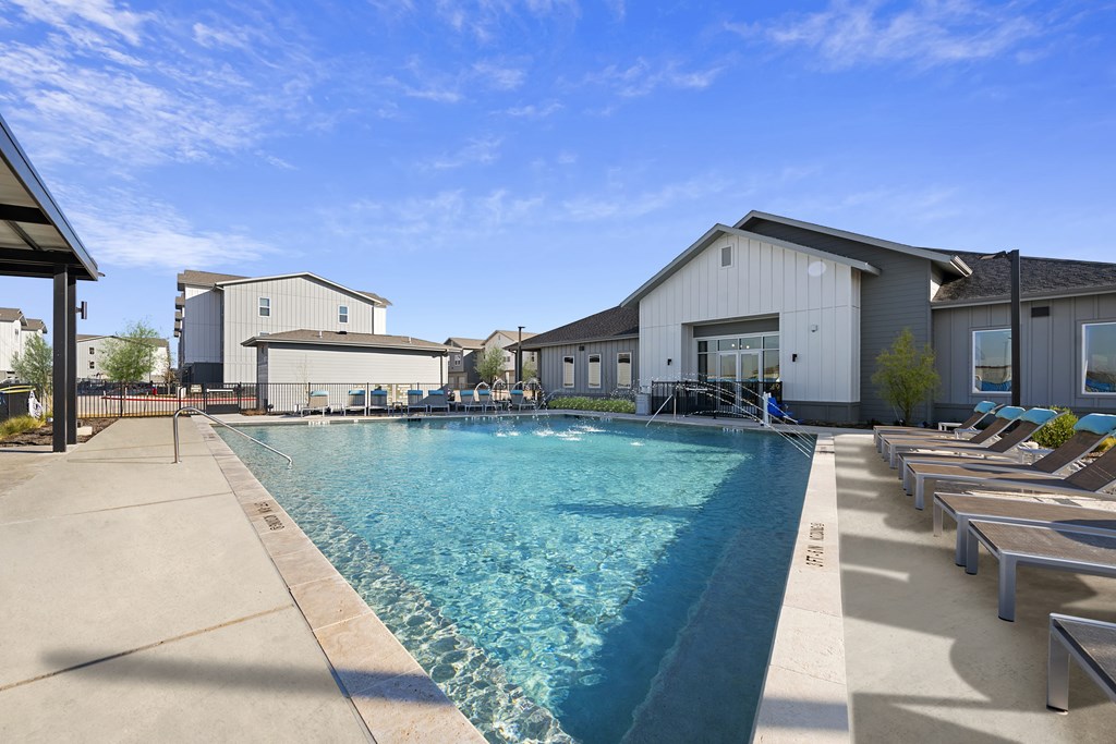 A large swimming pool with lounge chairs and a building in the background.