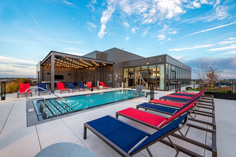a pool with red and blue lounge chairs in front of a building