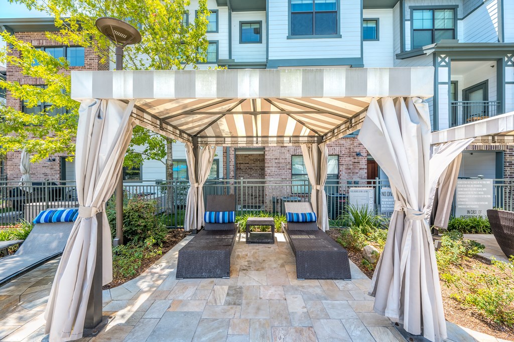 a pergola with lounge seating and a fire pit in front of an apartment building