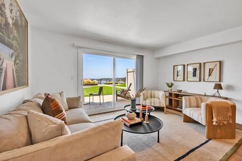 A living room with a couch, a chair, a coffee table, and a view of the outside.