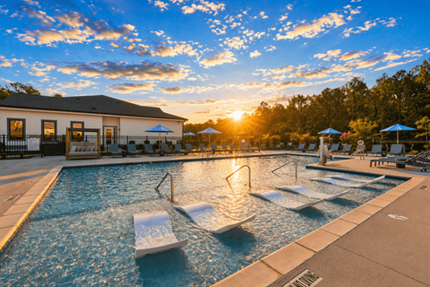 A sunset view of a pool with a building in the background.