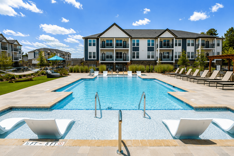 A large swimming pool with lounge chairs and a building in the background.
