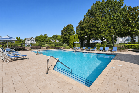 A swimming pool surrounded by a brick patio and lounge chairs.