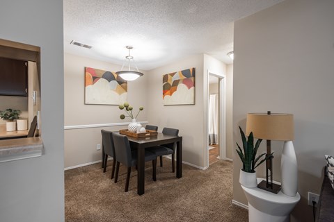 A dining room with a table set for two and a lamp on a side table.