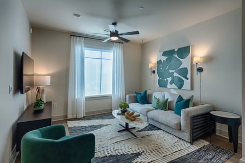 A living room with a grey couch, a green armchair, a coffee table, and a ceiling fan.