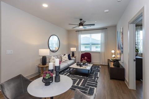A modern living room with a grey sofa, a round table, and a ceiling fan.