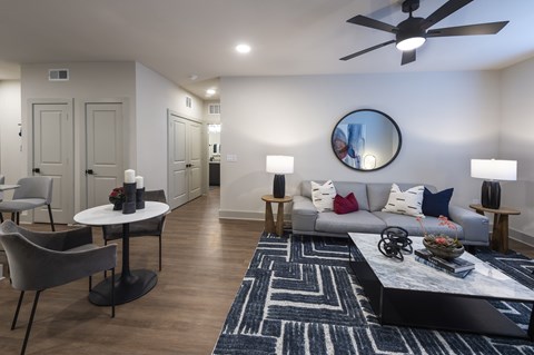 A modern living room with a grey couch, a round mirror, and a ceiling fan.