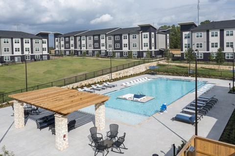 A pool with a wooden deck and lounge chairs in front of apartment buildings.