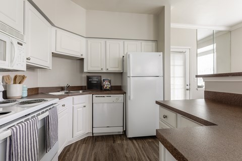 A white refrigerator is in the middle of a kitchen with white cabinets.