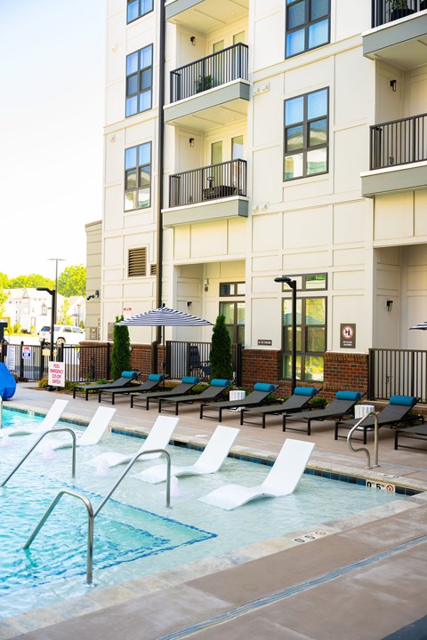 A pool area with chairs and a building in the background.