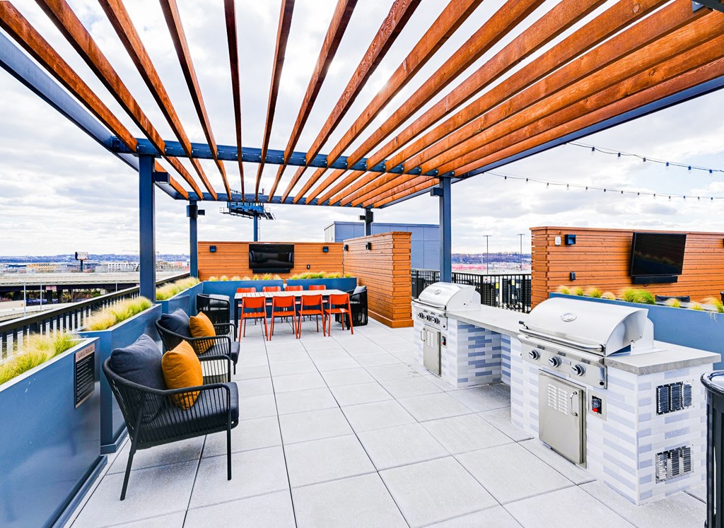A patio with a grill and chairs under a wooden pergola.