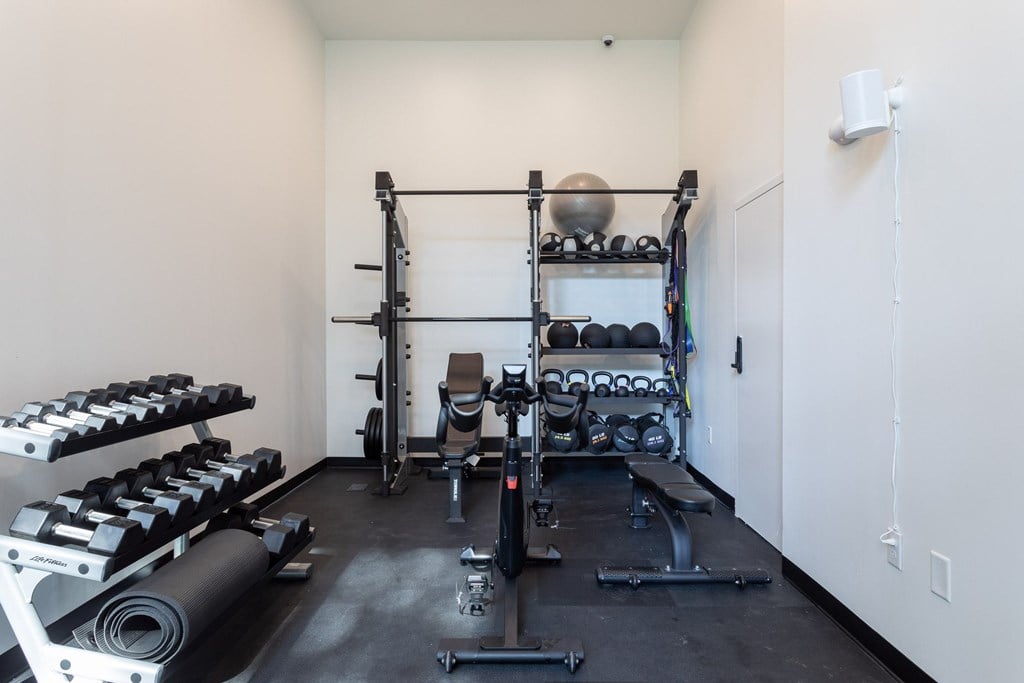 A gym with a variety of equipment including dumbbells, weight plates, and a bench press.