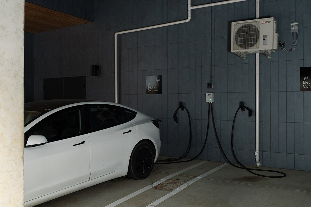 A white car is parked in a garage connected to an electric car charging station.