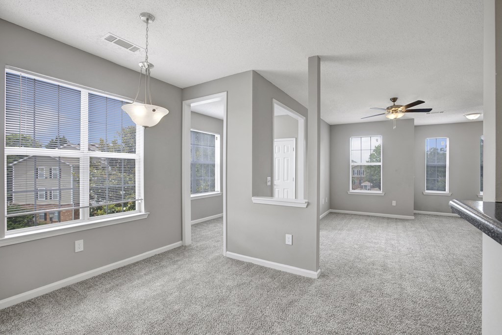 A well-lit, empty room with a ceiling fan and carpeted floor.