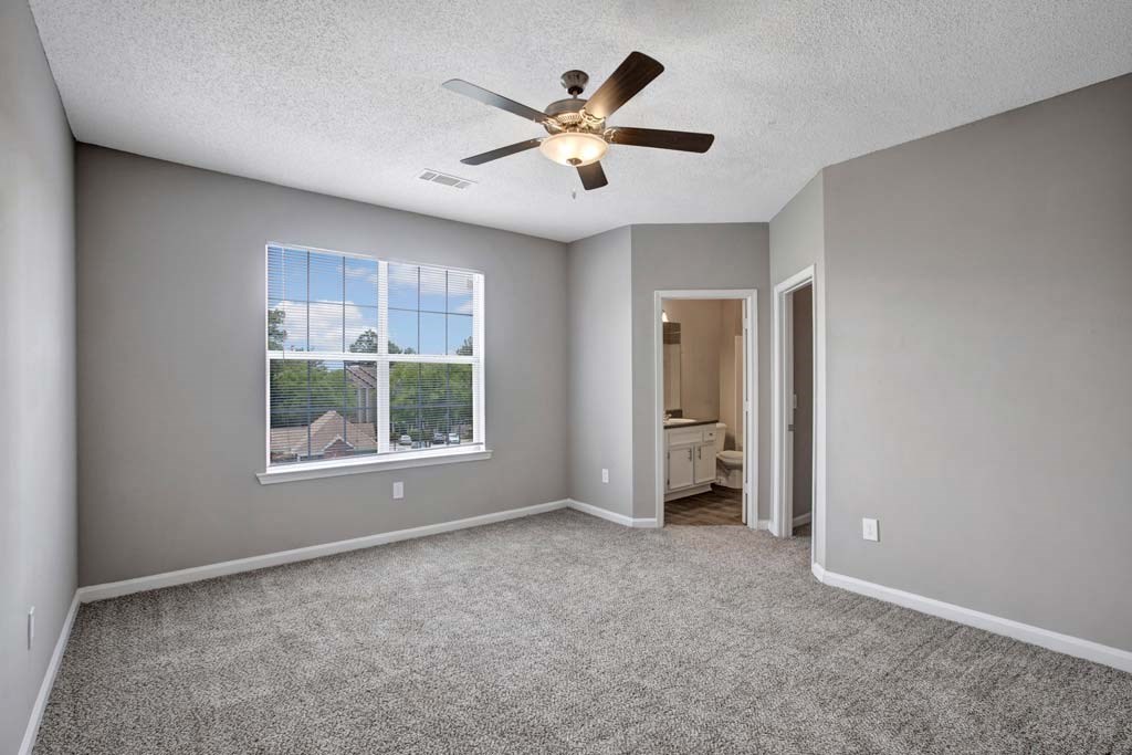 A room with a ceiling fan and a window showing a view of a house.
