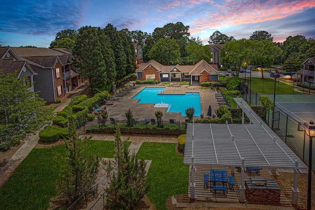 A pool surrounded by a fence and a patio area with chairs.