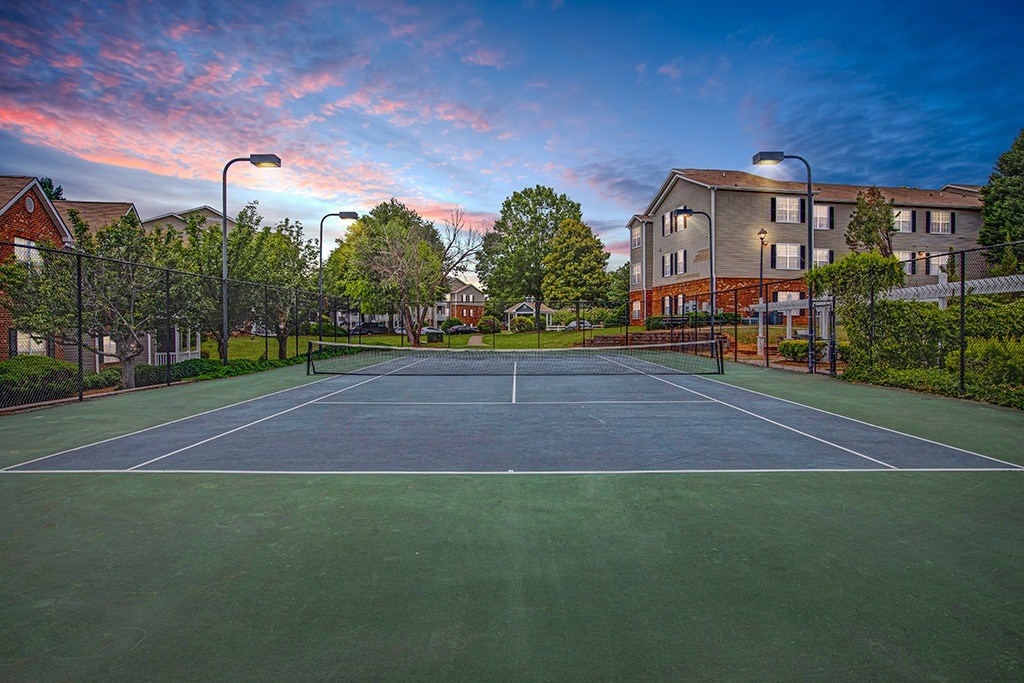 A tennis court is surrounded by a fence and a building.