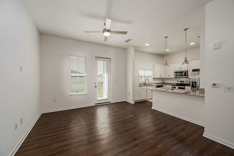 an empty living room with a kitchen and a ceiling fan