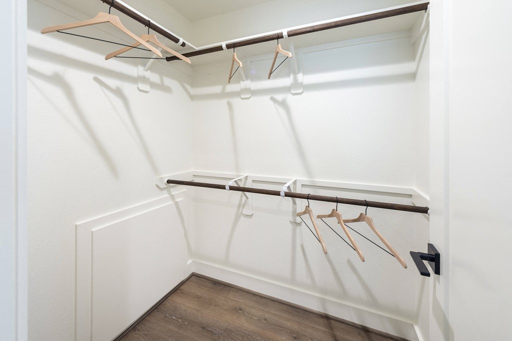 a walk in closet with white walls and wood flooring