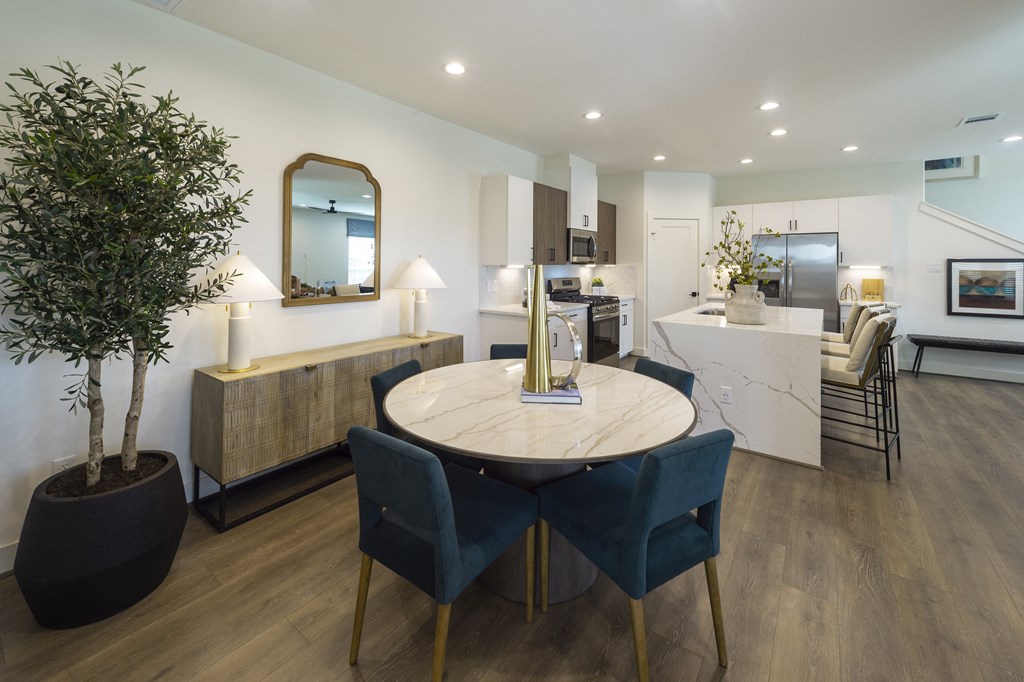 a dining area with a round table and blue chairs and a kitchen in the background
