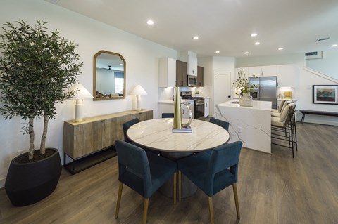 a dining area with a round table and blue chairs and a kitchen in the background