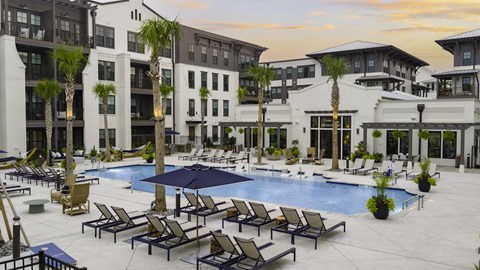 A large pool surrounded by lounge chairs and umbrellas in front of a multi-story building.