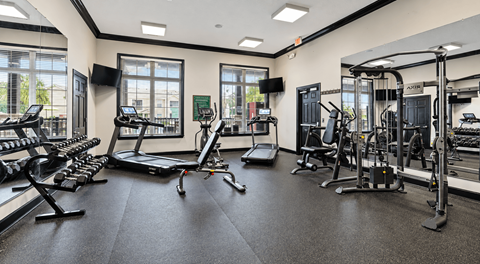 A spacious gym with various exercise equipment and a large mirror on the wall.