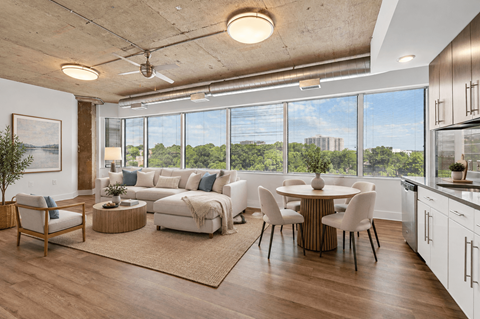 A well-lit, modern living room with a view of the outdoors through large windows.