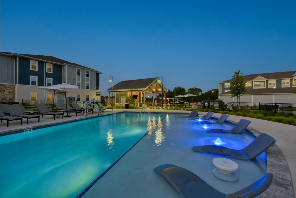 a swimming pool with chairs at night at an apartment complex