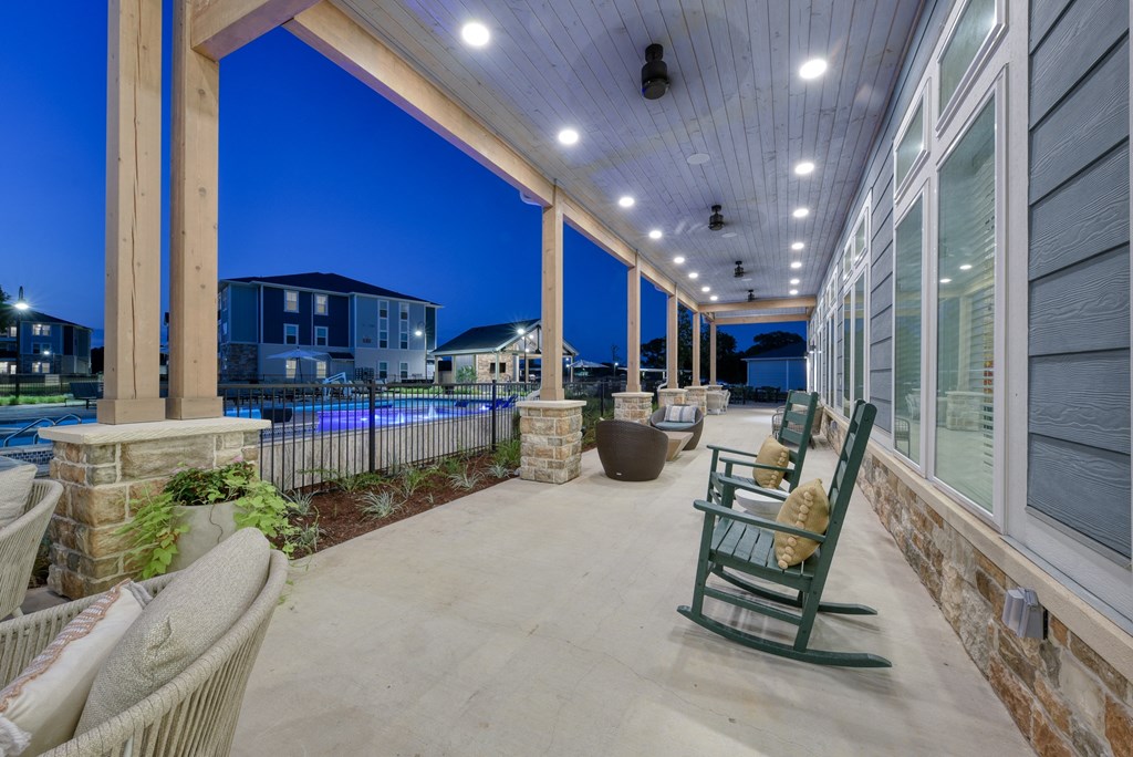 a covered porch with rocking chairs and a pool at night