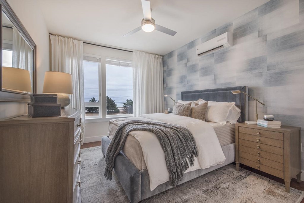 Furnished bedroom with ocean views, accent wall, ceiling fan and dresser